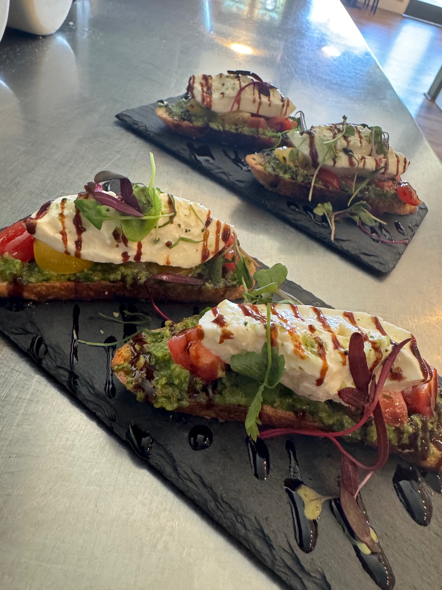 Burrata and pesto crostini with heirloom tomatoes and balsamic on slate