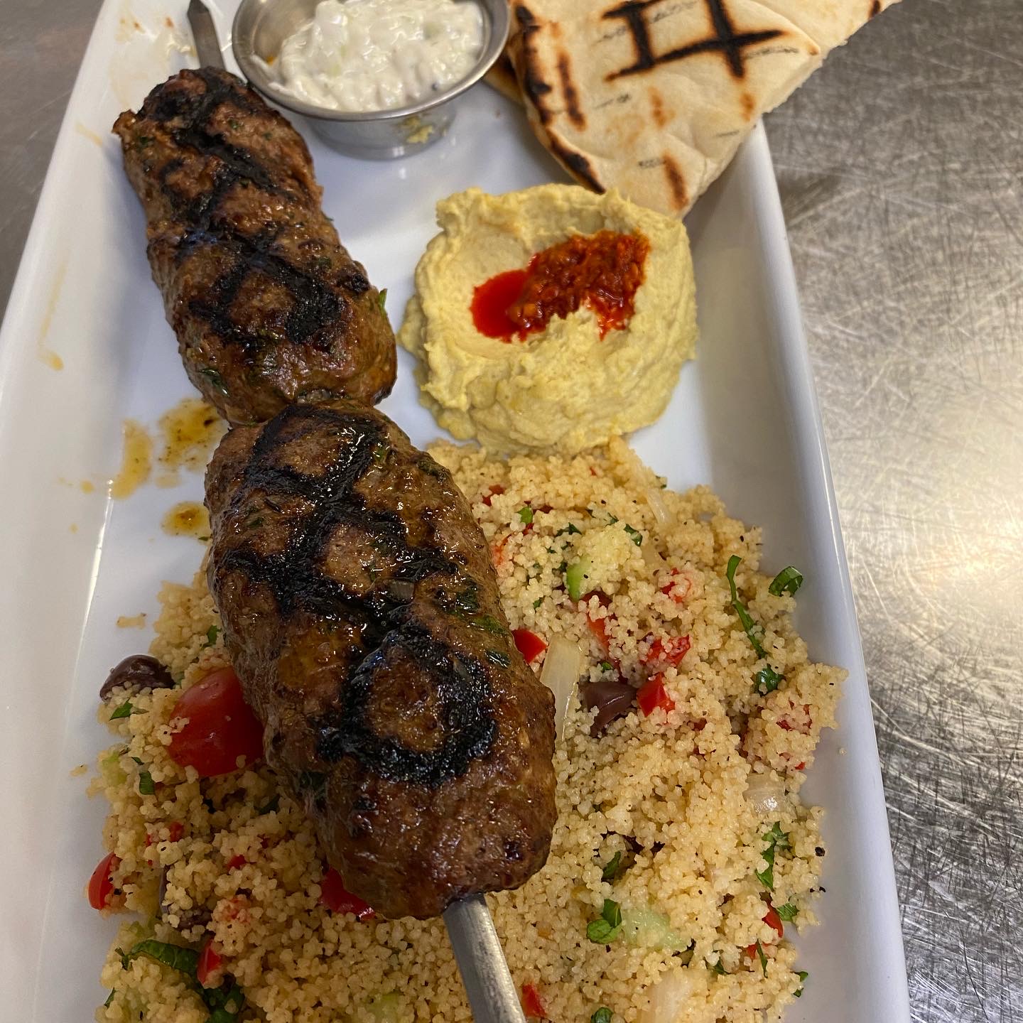 Grilled lamb kofta skewers with couscous salad, hummus, tzatziki, and charred flatbread