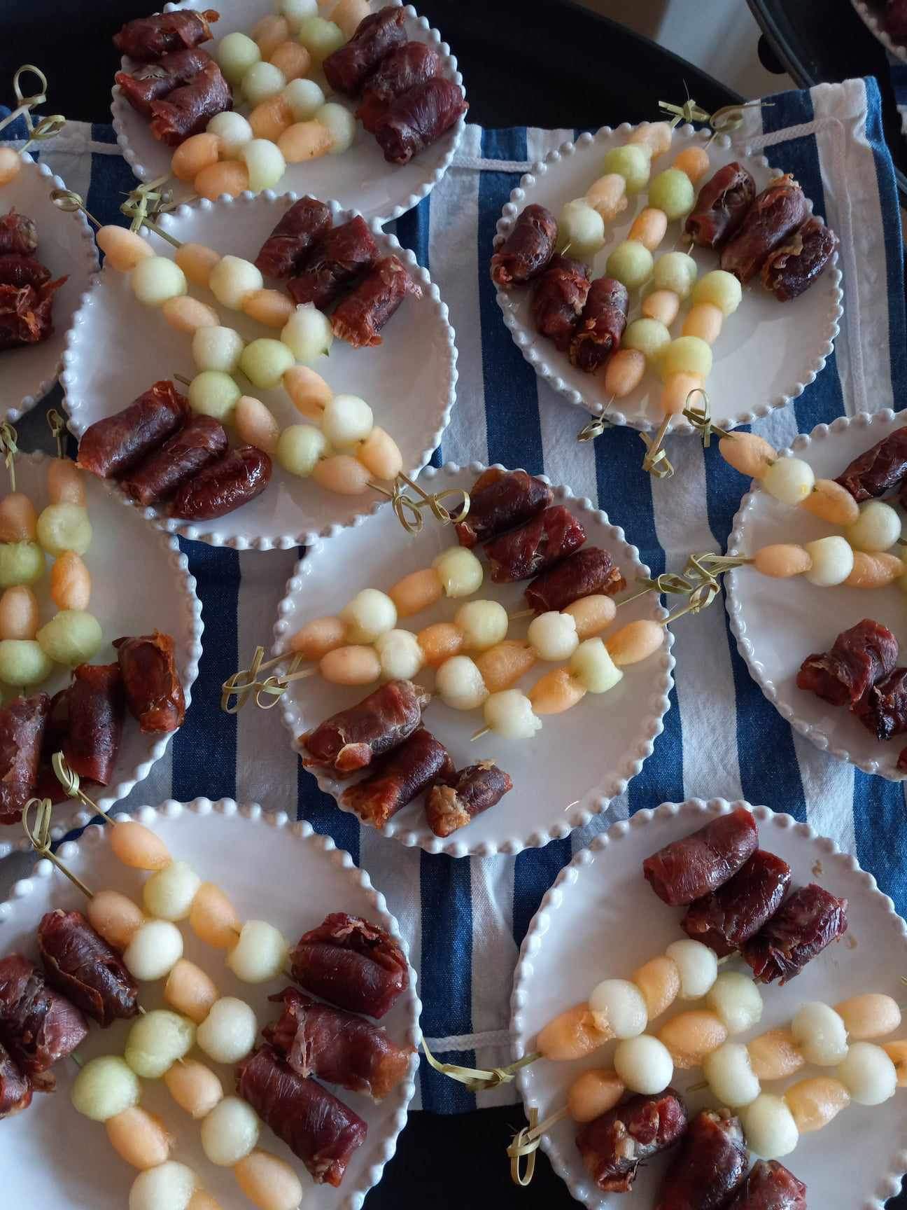 Individual plates of melon skewers with prosciutto-wrapped dates